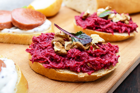 Breakfast sandwiches with boiled grated beets and walnuts on a piece of white baguette on a cutting board.の写真素材