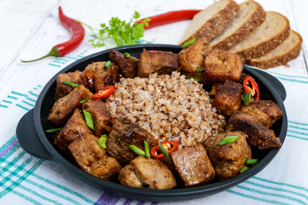 Buckwheat porridge with pieces of fried pork, served on a cast-iron frying pan.の写真素材