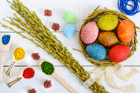 Colorful painted eggs in a nest of twigs of willow on a light background and multicolored rice for decorative painting. Traditionally for Easter. The top viewの写真素材