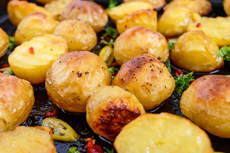 Baked potatoes with a golden crust on a black background with hot pepper, garlic, spices and herbs. Close-up.の写真素材