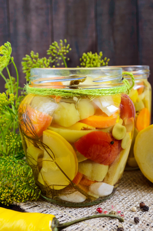 Pickles: vegetable assortment (zucchini, pepper, carrots, tomato, green peas) in glass jars on a dark wooden background.の写真素材