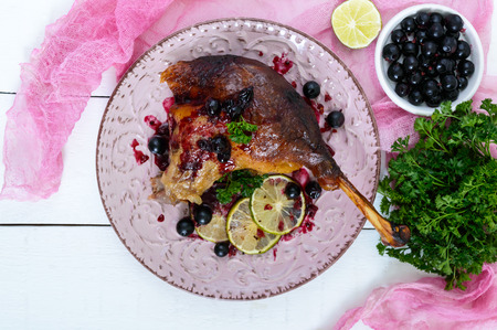Baked goose leg in berry sauce on a ceramic plate on a white wooden background. Top view.の写真素材