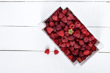 Fresh juicy pink raspberry in a wooden box on a white background. Top view. Harvest.
