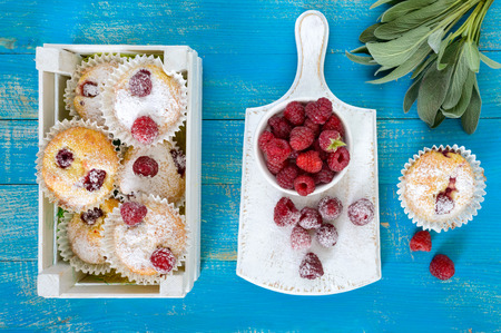 Curd cakes (muffins) with raspberries, decorated with powdered sugar. Serve in a white wooden box. Fresh raspberries in a ceramic bowl. Top view.の写真素材