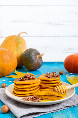 Fragrant golden pumpkin pancakes with honey and walnuts on a blue wooden background. Traditional American dishの写真素材