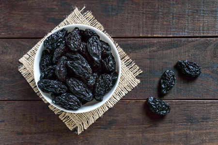 Prunes in a ceramic bowl on a dark wooden background. Dried fruits. The top viewの写真素材