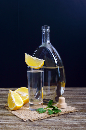 Vodka or tequila in shot glasses and in the bottle with lemon sliÑe on rustic wooden background. Traditional strong drink. Close-up. Vertical viewの写真素材