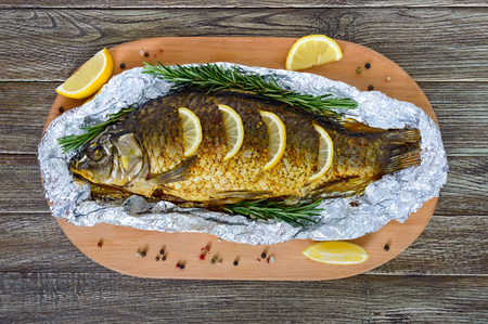 Large baked carp with herbs, lemon and spices in foil on a wooden background. Top viewの写真素材