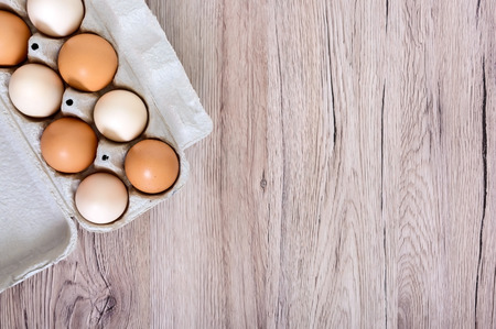 Fresh raw chicken eggs in carton egg box on wooden background. The top view on brown and white eggs. Close-up view. The main ingredient for many dishes. Free space for inscriptions, notes.の写真素材