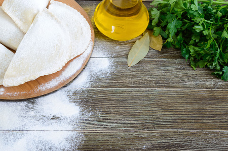 Not fried chebureks in flour on a wooden table. Traditional Turkic-Mongolian dish. Frozen semi-finished products. Free space for an inscription.の写真素材