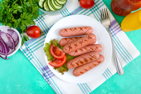 Delicious juicy grilled sausages on a plate, vegetables, ketchup and mustard on a bright background. The top viewの写真素材