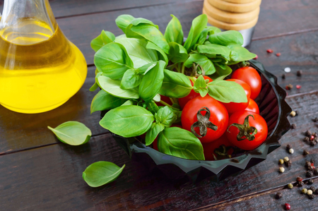 Green fresh leaves of organic basil and small ripe tomatoes, oil and pepper on a wooden background for a healthy diet.の写真素材