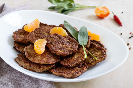 Tasty liver cutlets with tangerines on a white plate on the table.の写真素材