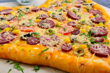 Tasty pizza in a heart shape with mushrooms, salami, pepperoni, olives, corn. Close upの写真素材