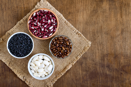 Assortment of colorful raw beans in bowls on a wooden table. Healthy food, dieting, nutrition concept. Legumes - vegan protein source.の写真素材