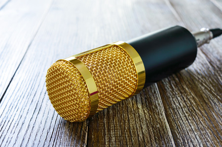Condenser gold microphone  on a wooden table. The light from left side. Musical theme.の写真素材
