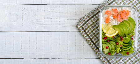 Lunch box: rice, salmon, salad with cucumber, avocado, greens on a white wooden background. Fitness food. The concept of healthy eating. School lunch boxの写真素材