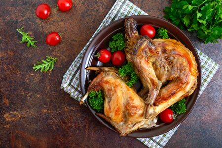 Whole baked rabbit with greens and tomatoes on a plate. Tasty dietary meat. Top view, flat lay.の写真素材