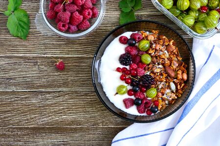 Yogurt, granola, fresh berries in a bowl on a wooden table. Delicious and healthy breakfast. Proper...