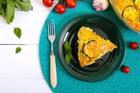 Zucchini, cheese, eggs, cream and greens casserole on a white wooden background. Portion of...