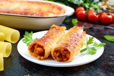 Stuffed cannelloni with bechamel sauce. Cannelloni pasta baked with meat, cream sauce, cheese on a black backgroundの写真素材