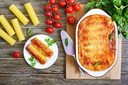 Stuffed cannelloni with bechamel sauce. Cannelloni pasta baked with meat, cream sauce, cheese on a wooden background. Top view, flat lay.の写真素材