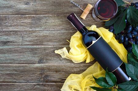 Wineglasses with red wine, bottle, corkscrew, blue grapes, leaves on a wooden table. Wine background with copy space. Top view, flat layの写真素材