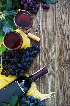 Wineglasses with red wine, bottle, corkscrew, blue grapes, leaves on a wooden table. Wine background with copy space. Top view, flat layの写真素材