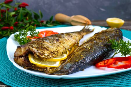 Baked herring with lemon and spices on a white plate on a wooden table. Tasty fish dish. Top view.