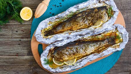 Baked herring with lemon and spices in foil on a wooden table. Tasty fish dish. Top view.