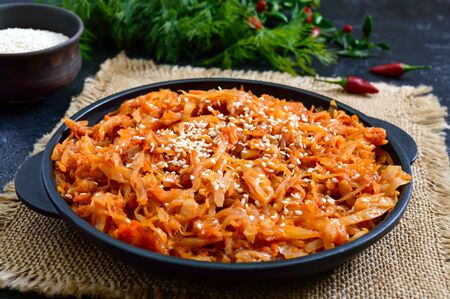 Braised cabbage from tomato sauce in a cast-iron frying pan on a black background. Lenten menu. Diet...