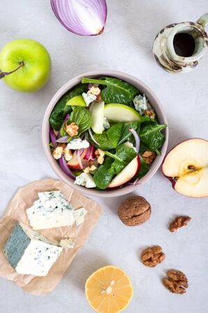 Delicious diet fitness salad with spinach, apples, red onions, blue cheese, nuts. Proper nutrition. Light concrete background. Top view.の写真素材