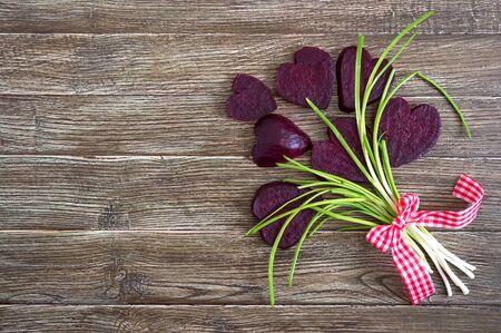 A bouquet of flowers from slices of boiled beets and green onions on a wooden background. To love...