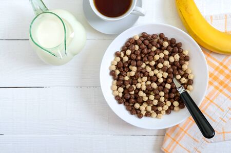 Wholegrain chocolate and milk balls, fruit, tea and milk on white wooden background. Healthy cereal...