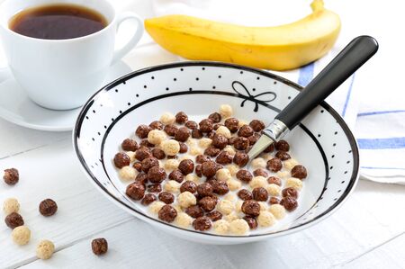 Wholegrain chocolate and milk balls, fruit, tea and milk on white wooden background. Healthy cereal breakfast. Baby breakfast. Baby eating. Balanced diet.の写真素材
