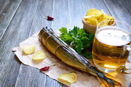 Beer snacks. Smoked fish, chips, a glass of lager beer on a wooden table.の写真素材