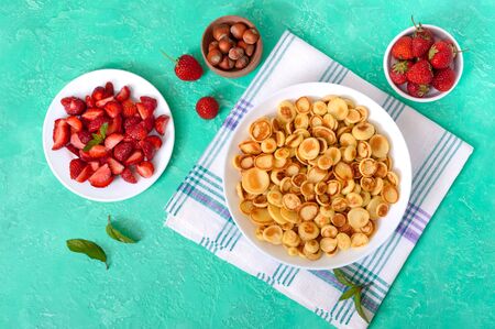 Pancake cereal in a bowl with fresh strawberries and nuts on a bright background. Tasty and trendy breakfast. Organic Dutch Mini-Pancakes. Foods trend. The top viewの写真素材