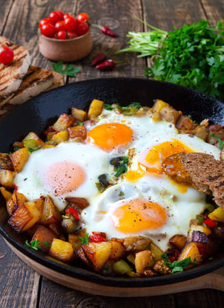 Fried eggs with vegetables - shakshuka in a frying pan and rye bread on an old wooden background....