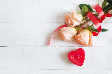 Bouquet of roses and a candle-heart on a white wooden background. The concept of wedding, valentine's day, birthday. Floral background with copy space. Top view.の写真素材