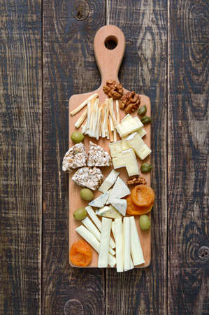 Different kinds of cheeses, dried apricots, whole-grain breads, nuts, olives, capers on a wooden board. Cheese board, snacks. The top viewの写真素材