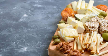 Different kinds of cheeses, dried apricots, whole-grain breads, nuts, olives, capers on a wooden board. Cheese board, snacks. Copy spaceの写真素材