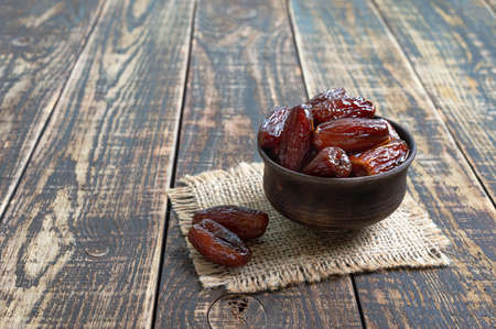 Organic sun dried dates in a bowl on old wooden table.