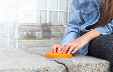 Girl with Pop up game playing outdoors. Kid hands playing with silicone antistress toy. Great fun on vacation. Copy spaceの写真素材