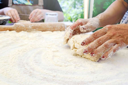 The cook teaches children to making dough. The female hand kneads the dough on a floured table. Master class in baking. Cooking at home. Copy spaceの写真素材