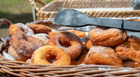 A pile of freshly baked donuts in powdered sugar are in a basket with serving tongs. Close-up. Selling donuts outdoors.の写真素材