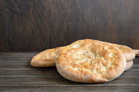 Simple unleavened flapjack. Round bread with sesame on a wooden background.