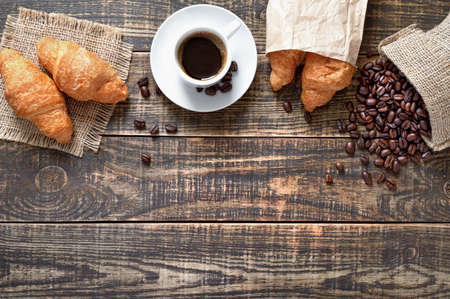 Coffee cup, freshly baked croissants, coffee beans on wood background - traditional breakfast concept with copy space. Top view, flat lay.の写真素材