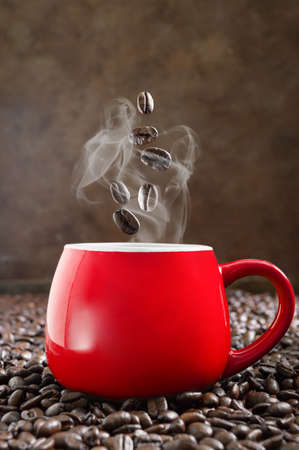 Roasted coffee beans fall into a red cup of hot espresso. The concept of a morning charge of cheerfulness and energy. Vertical viewの写真素材