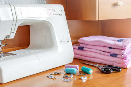 Sewing machine, textile, presser feet, threads, scissors on the table. Workplace of a seamstress.