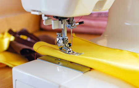 The sewing process on the sewing machine, close-up. The needle of a sewing machine with a red thread enters the yellow fabric, close-up.の写真素材